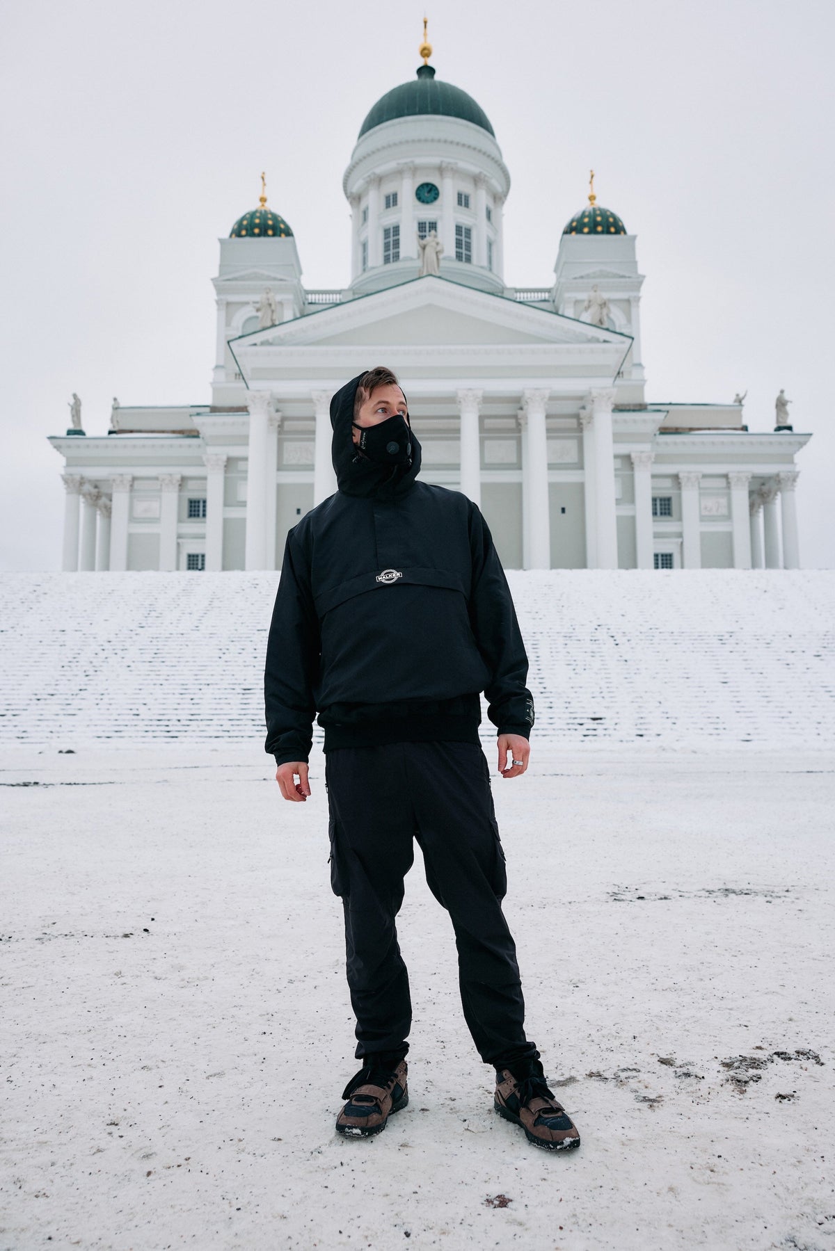 Alan Walker Core LV1 Windbreaker worn front on in snow by a masked fan outside a domed cathedral