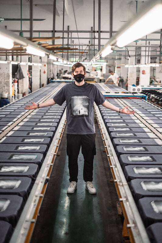 Alan Walker World of Walker Anniversary T-Shirt in grey worn by a masked model with arms spread in a factory hall