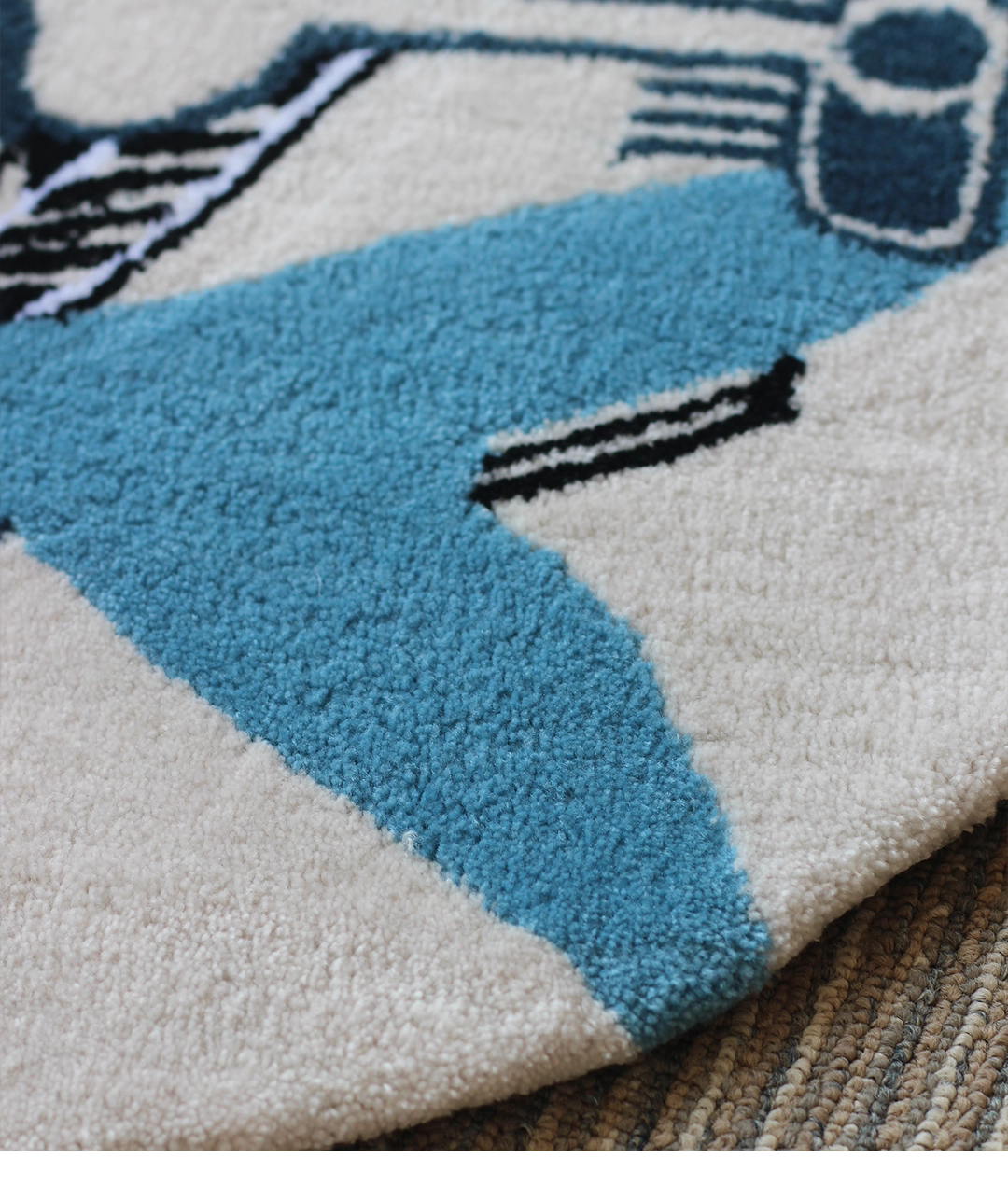 Alan Walker AV8 Rug edge detail, cream tufted border curving over a woven floor with blue graphic wing