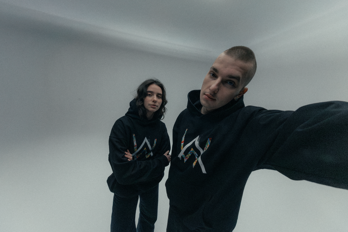 Alan Walker Tired Unity Hoodie on two models in a studio, matching black hoodies with colourful AW logos