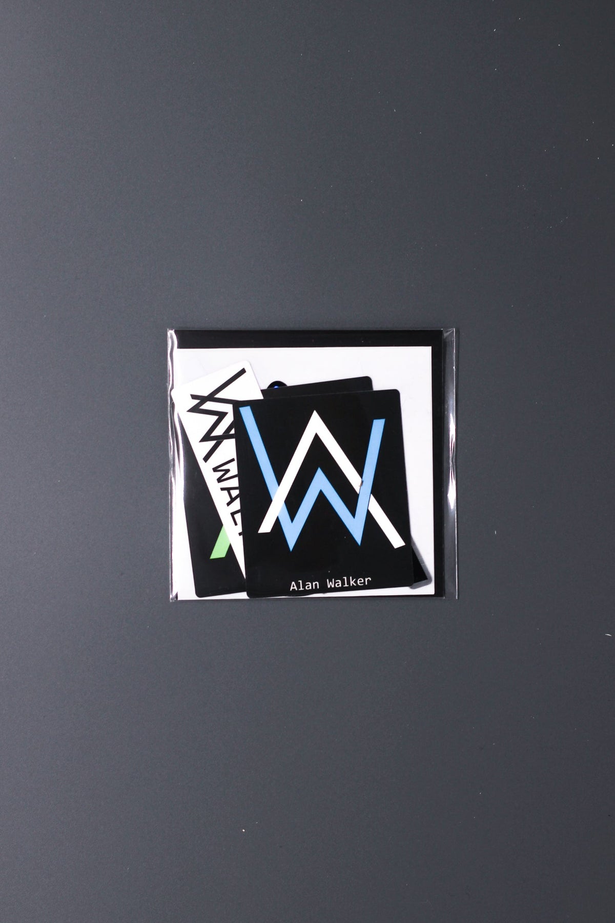 Alan Walker Logo Sticker Pack in its sealed clear sleeve, stacked AW logo decals visible through the packet
