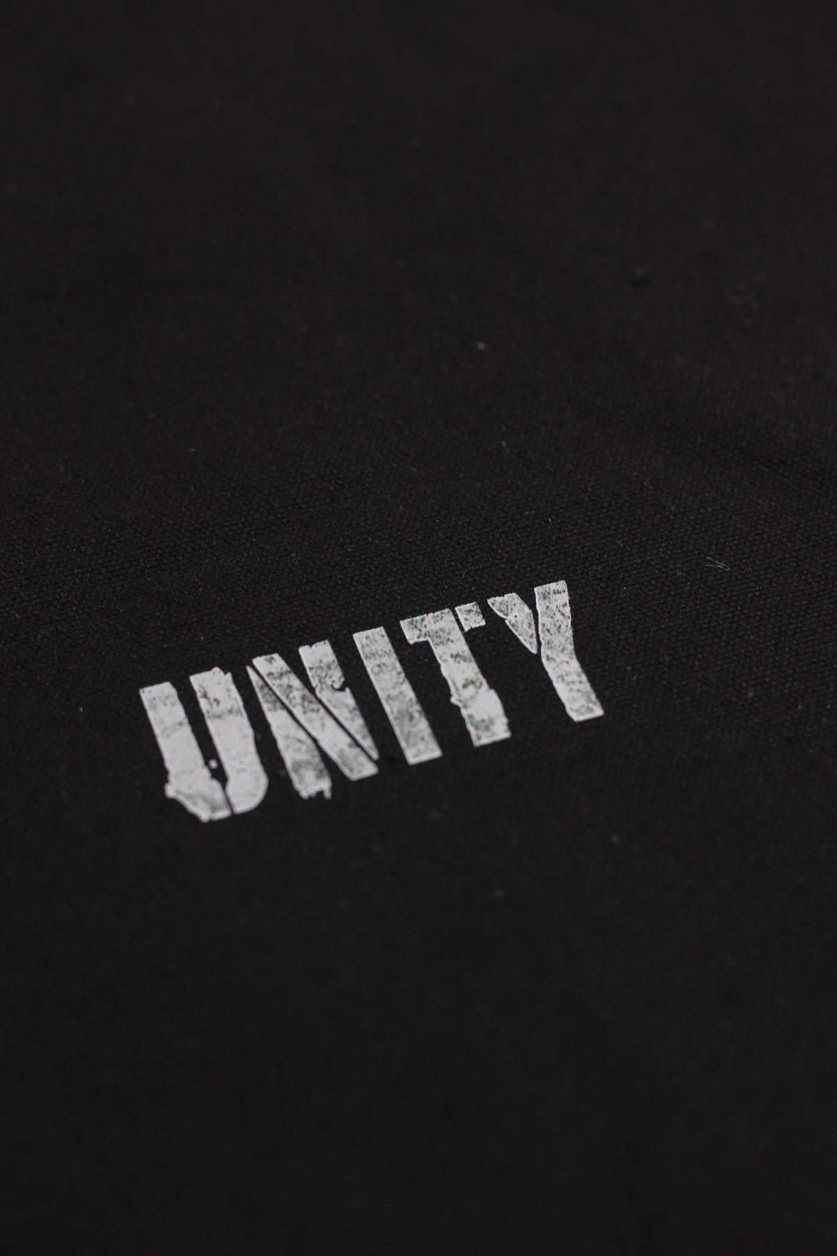 Alan Walker Tired Unity Tote print close-up, distressed white Unity lettering on black canvas