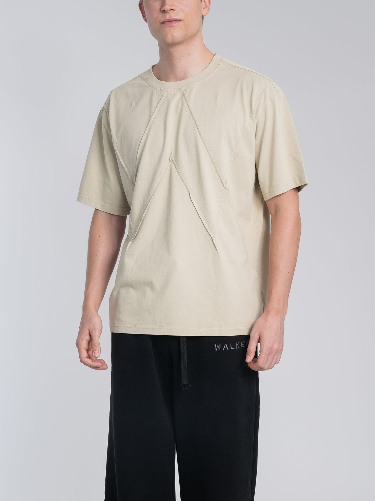 Alan Walker Stitch Logo Tee front view on a model, boxy beige tee with contour stitching forming the AW logo