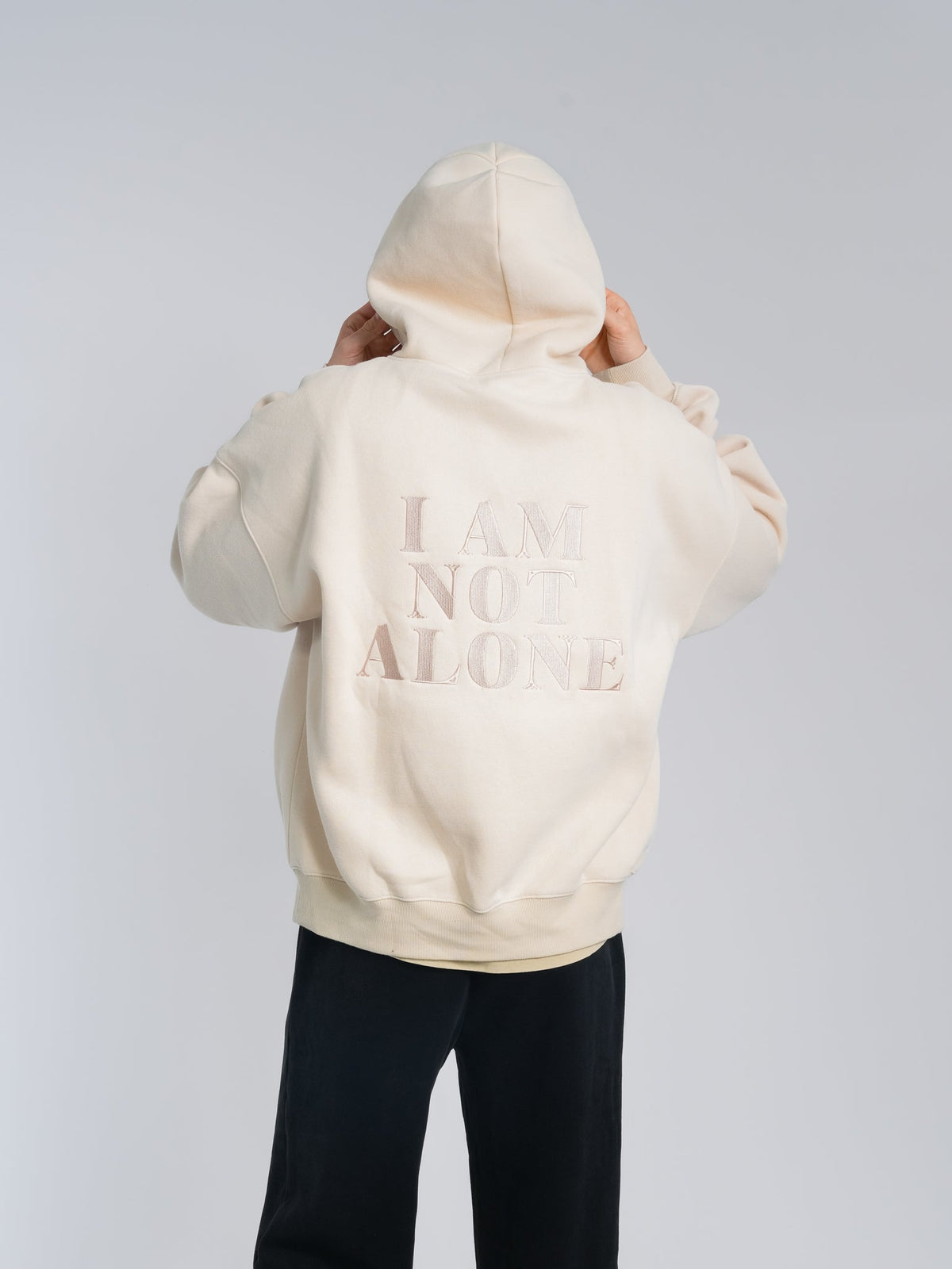Alan Walker Not Alone Hoodie in cream, back view on a model with tonal I Am Not Alone print and hood up