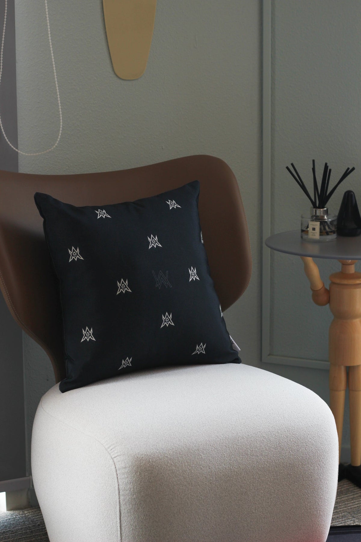 Alan Walker World of Walker Monogram Pillow styled on an armchair, black satin cushion with silver AW monogram print