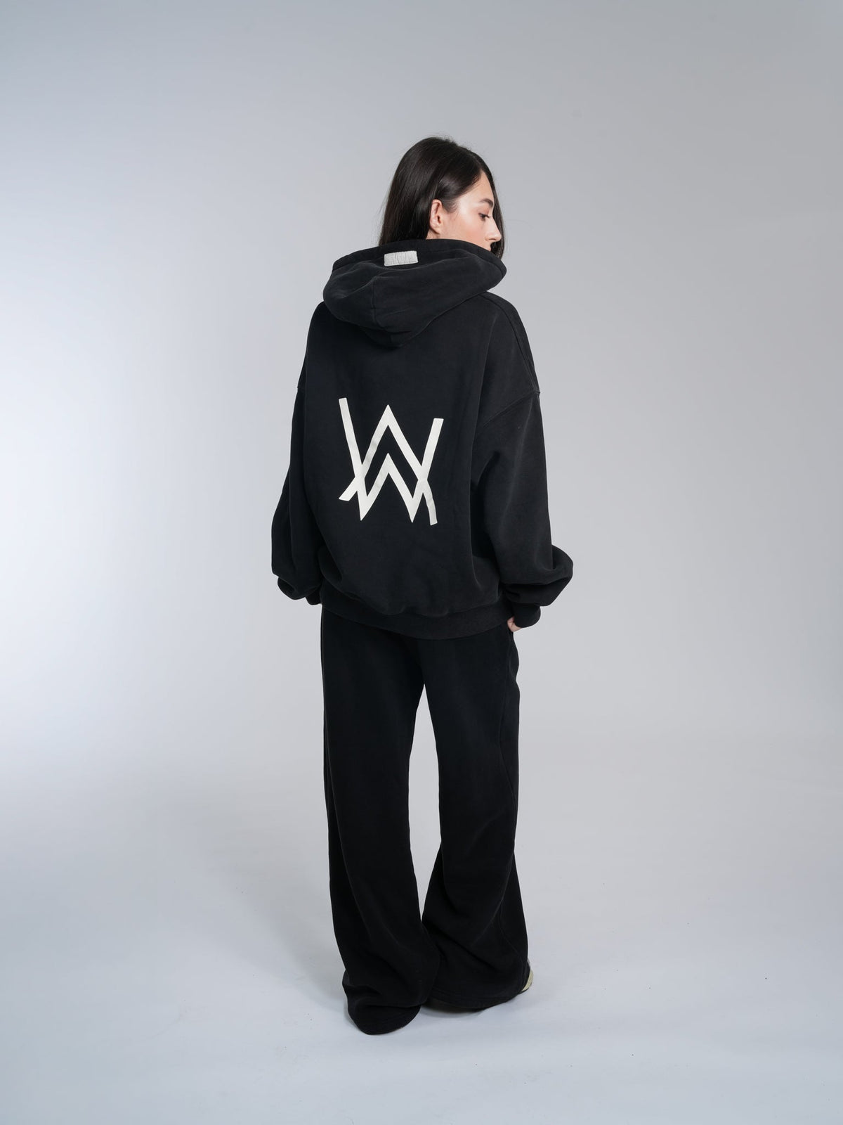 Alan Walker Core Hoodie back view on a female model, oversized black fleece with the white AW logo