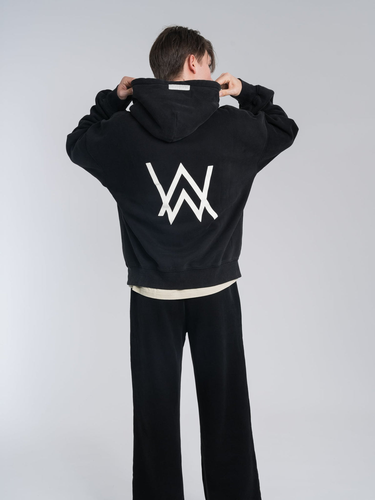 Alan Walker Core Hoodie worn by a male model, back view with the large white AW logo on black fleece