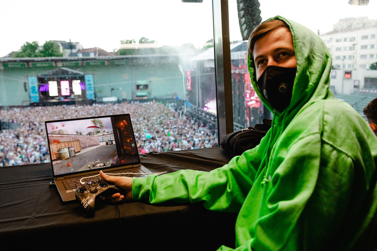 Alan Walker Stage Hoodie green worn at a festival, masked artist at a laptop above a packed crowd