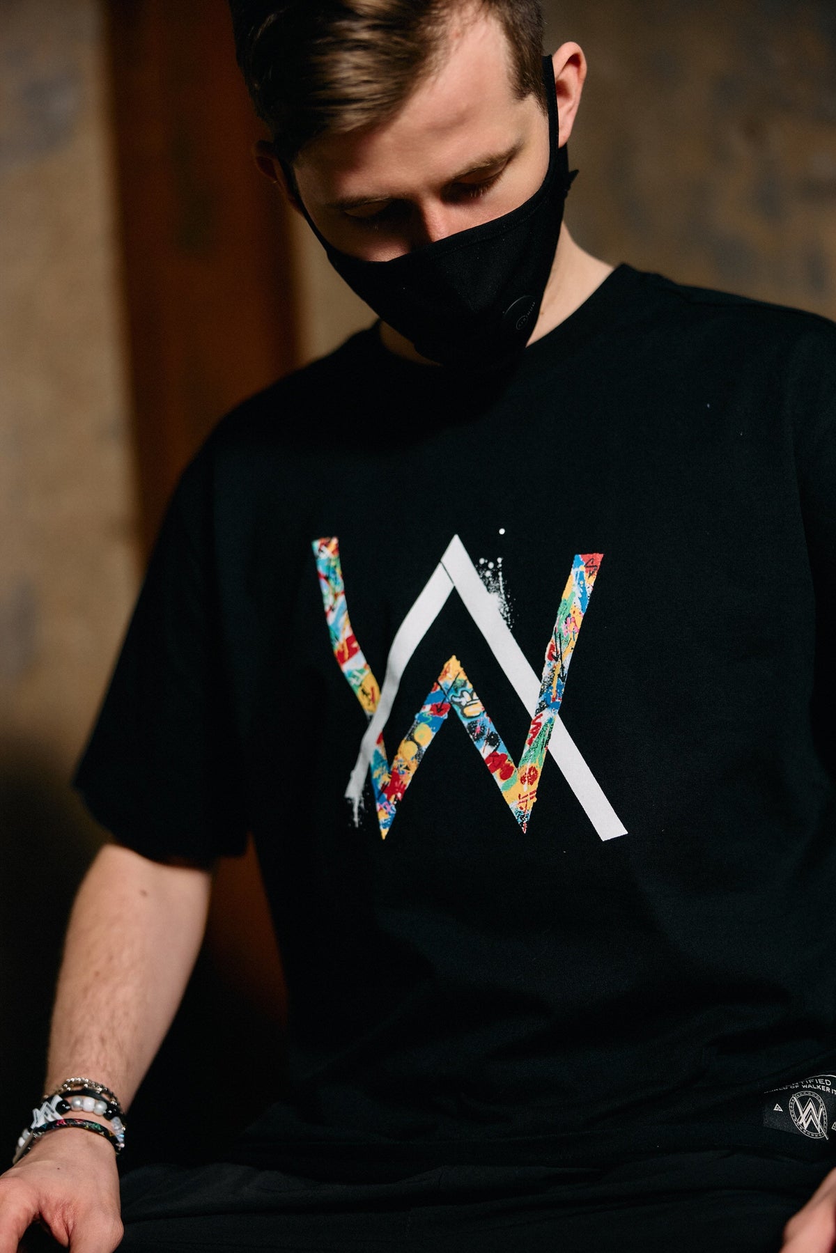 Alan Walker Tired Unity T-Shirt worn by a masked model, black tee with the multicoloured AW chest logo