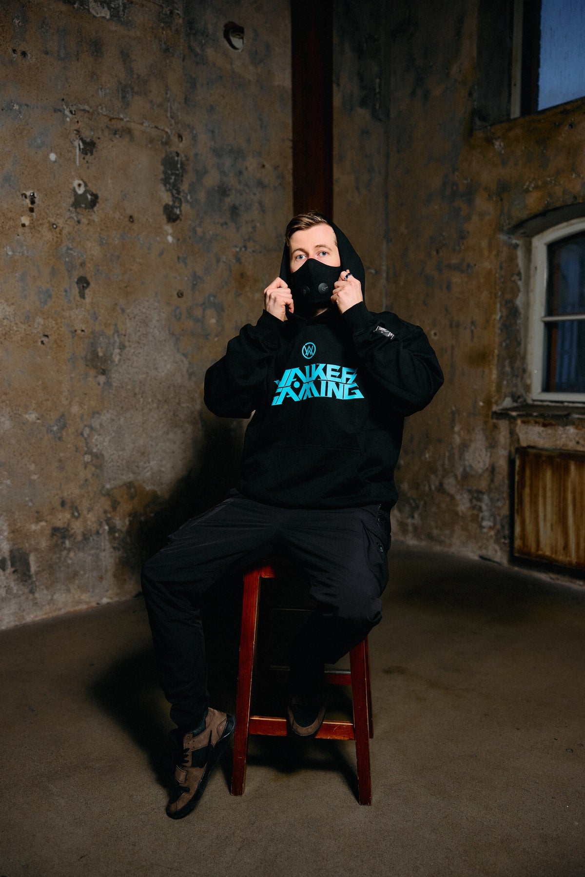 Alan Walker Gaming Hoodie worn by a masked fan seated indoors, blue Walker Gaming chest print on black