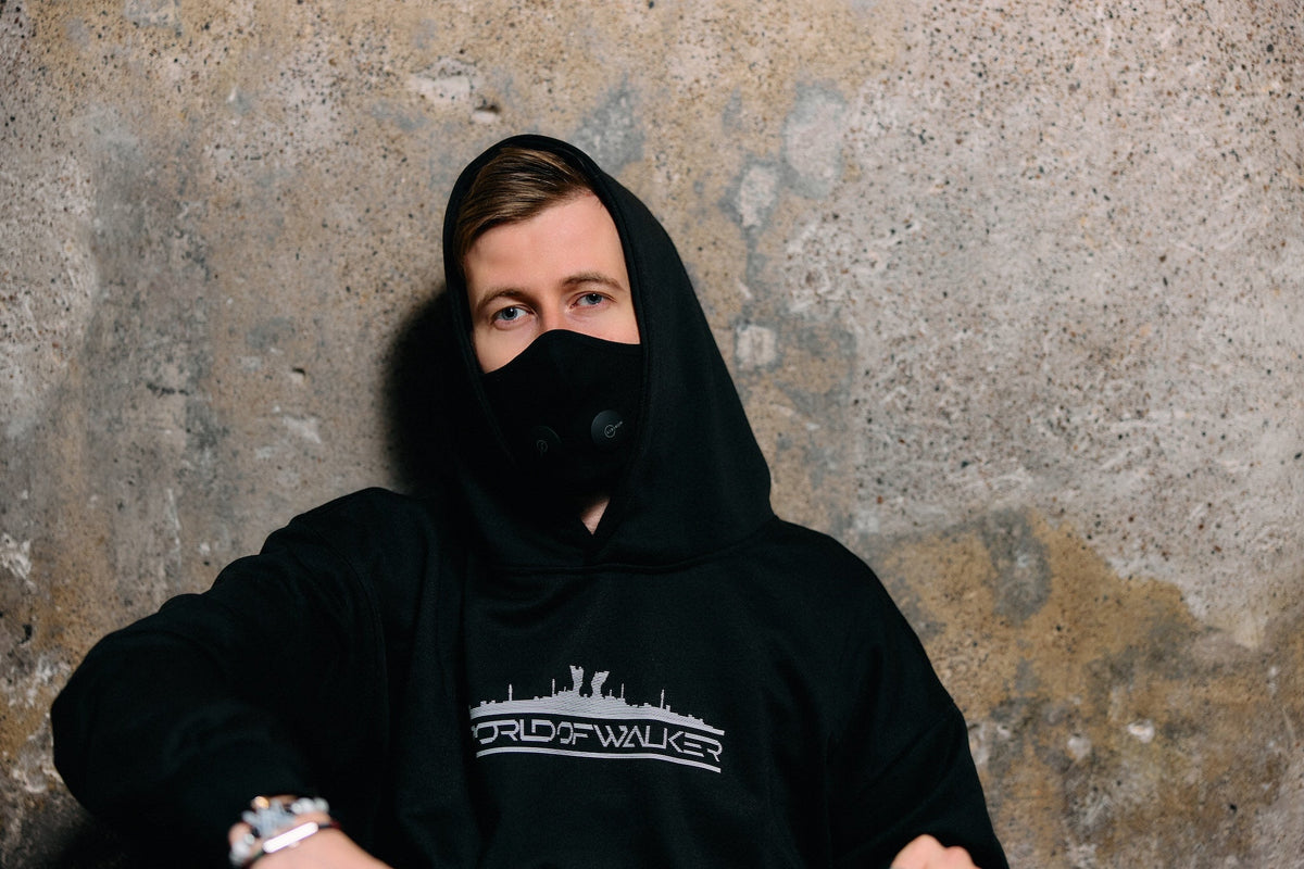 Alan Walker World of Walker Skyline Hoodie worn hood up by a masked model against a weathered concrete wall