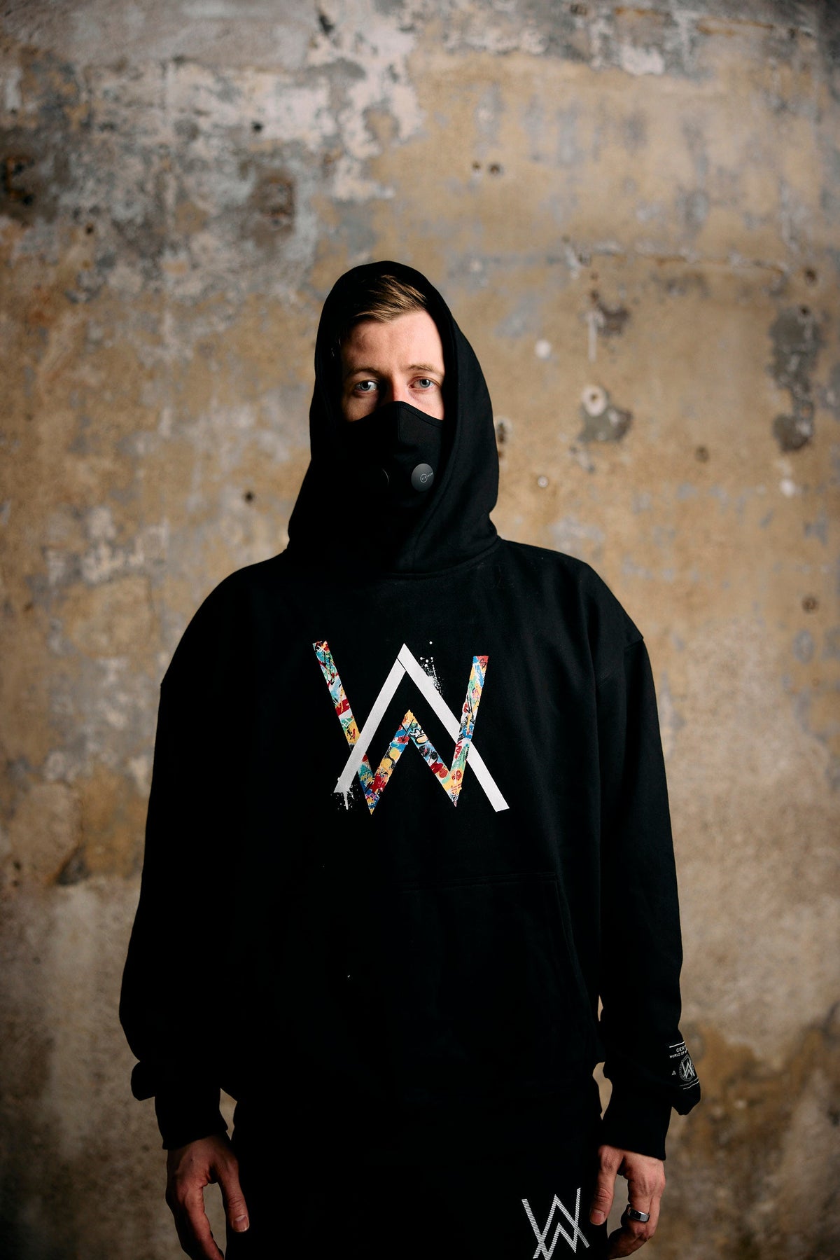 Alan Walker Tired Unity Hoodie worn hood-up by a masked model, black hoodie with bright AW chest logo