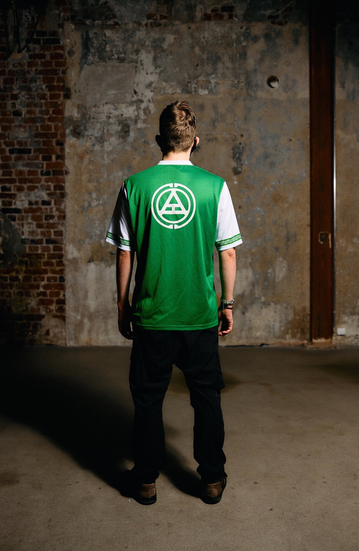 Alan Walker Creator Circle Tribe Jersey worn back view in a raw concrete room, green shirt with a white tribe circle print