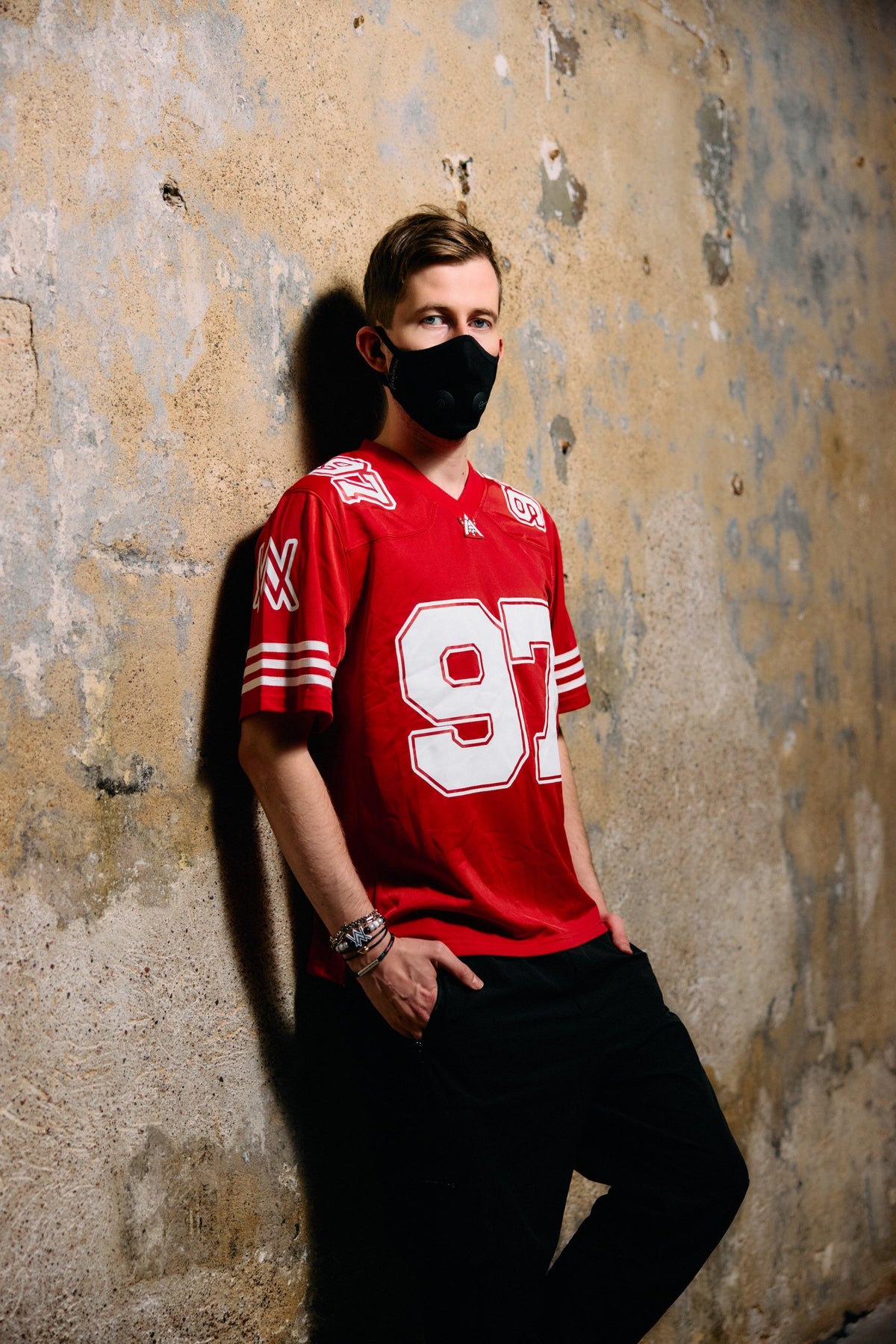 Alan Walker World of Walker 97 Jersey worn by a masked model against a stone wall, red jersey with white 97
