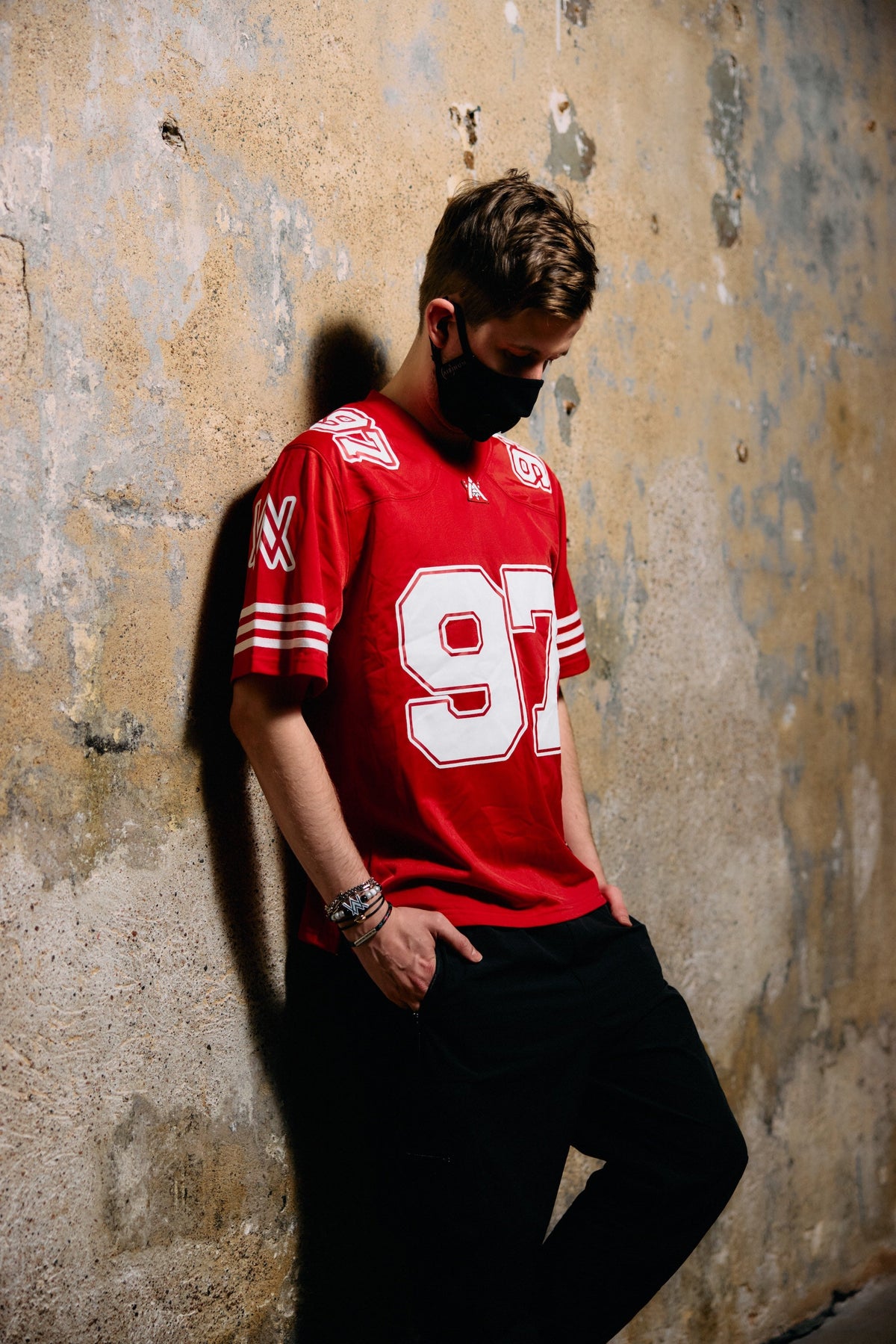 Alan Walker World of Walker 97 Jersey on a model leaning sideways, red mesh jersey styled with black pants