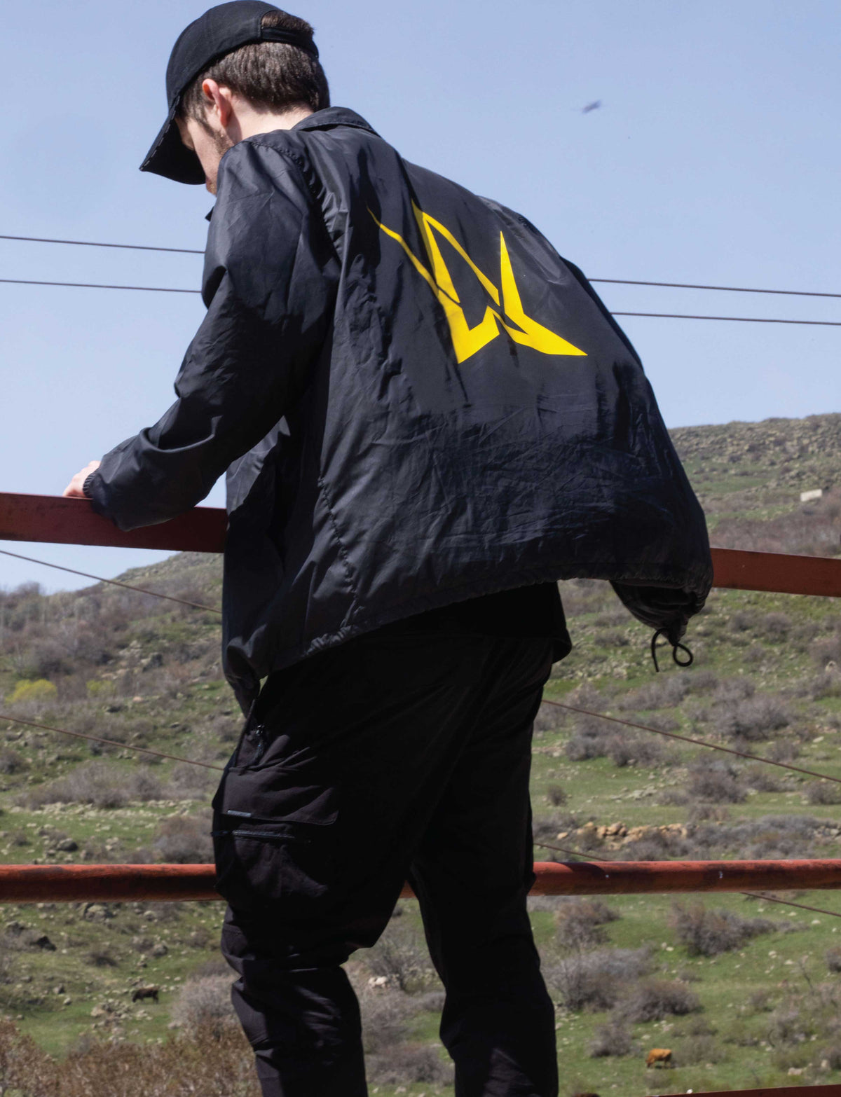 Alan Walker Walkerverse Crew Jacket worn by a model outdoors, black jacket with yellow AW logo across the back