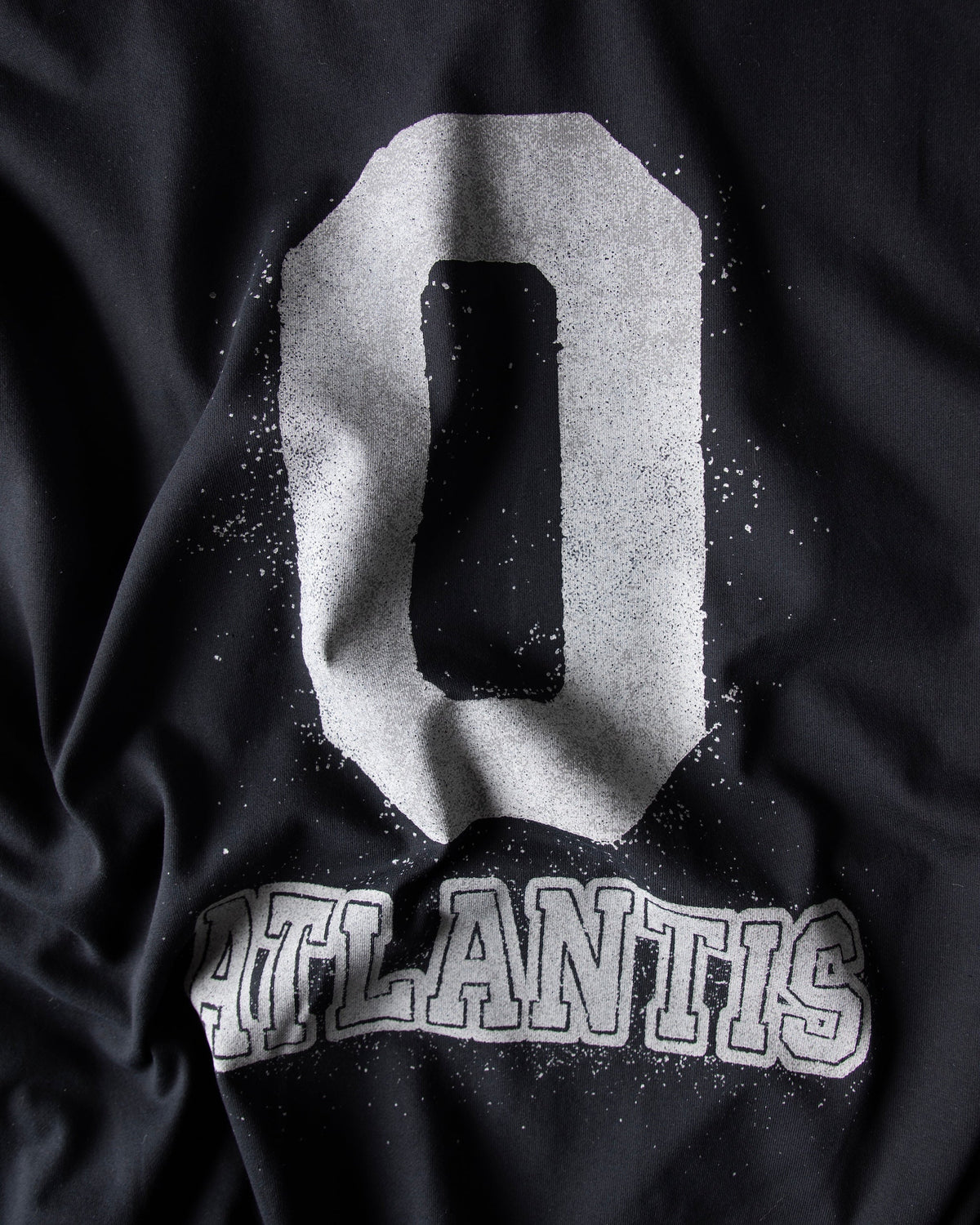 Alan Walker Atlantis 0 Hoodie fabric detail at an angle, textured white 0 and Atlantis print on black fleece