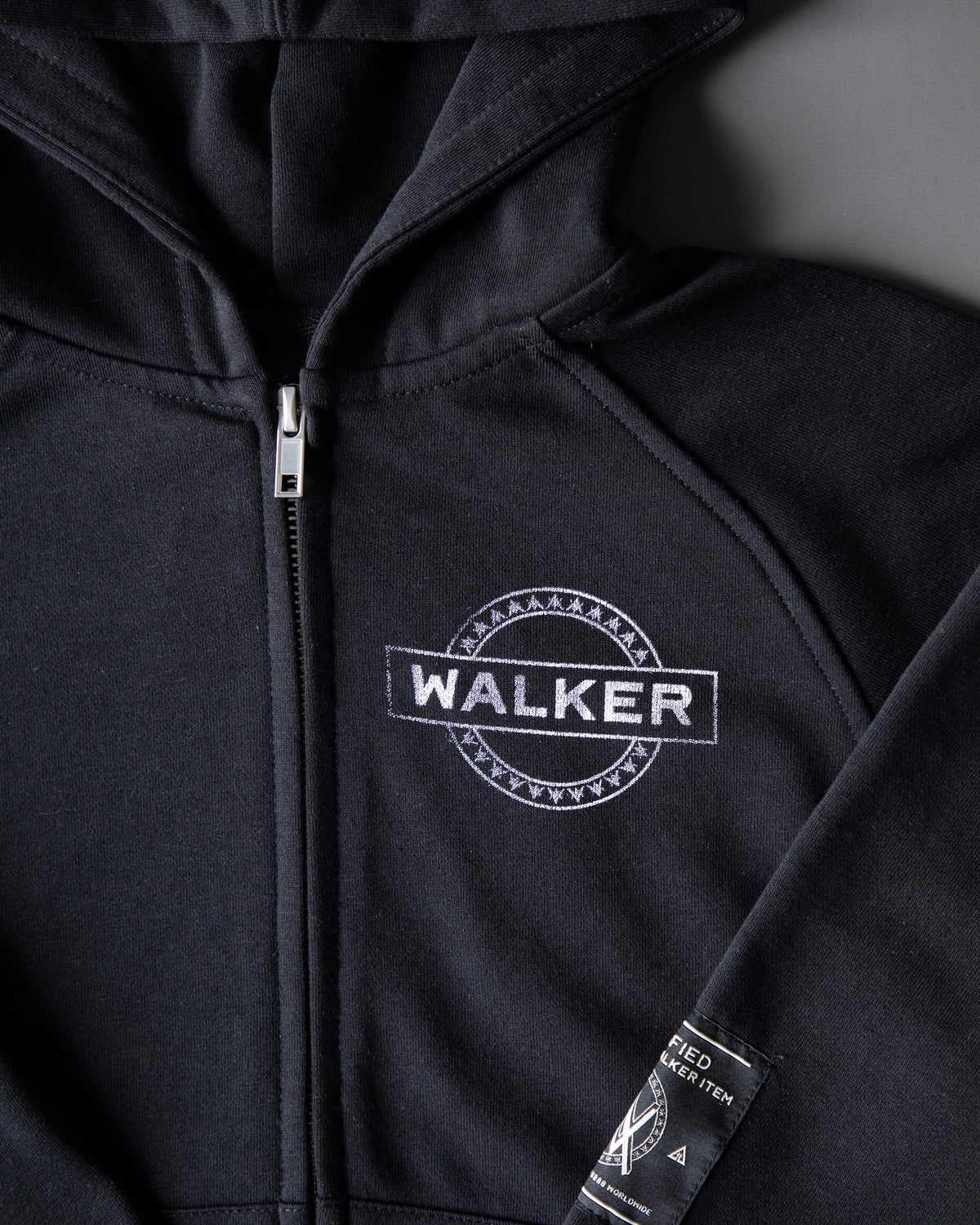 Alan Walker Monster Core Kids Zip Hoodie front detail, silver WALKER oval stamp beside the zip on black EDM streetwear