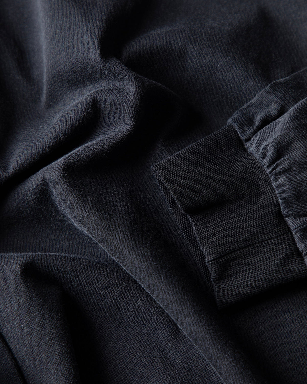 Alan Walker Heading Home Longsleeve fabric close-up, soft black cotton draped beside the ribbed sleeve cuff