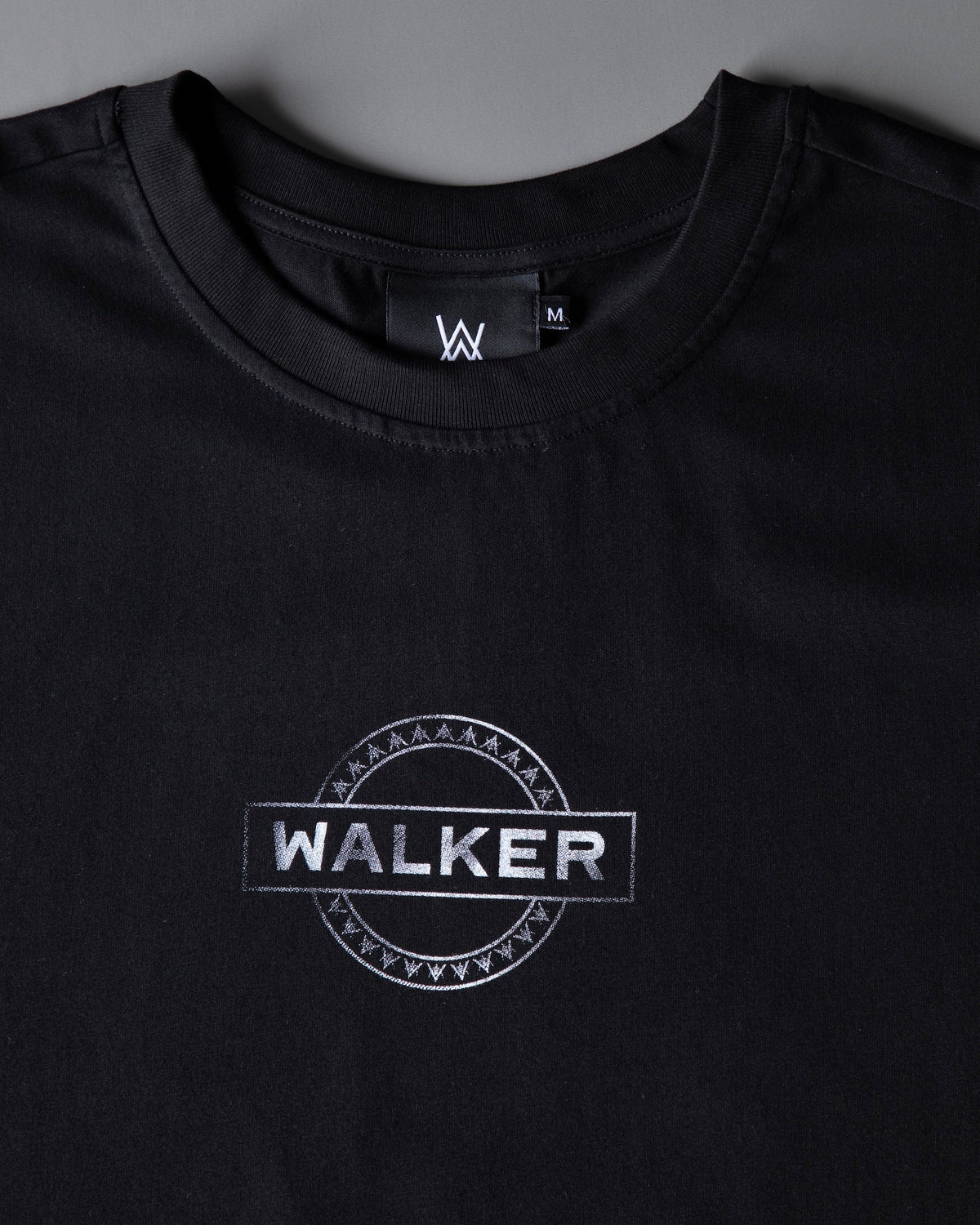Alan Walker Monster Core T-Shirt chest close-up, silver WALKER circle emblem printed below the AW neck label