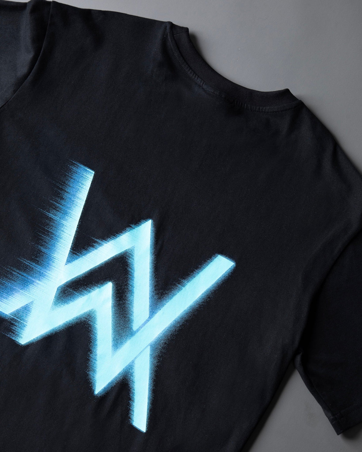 Alan Walker WRL Speed Logo T-shirt back print close-up, glowing blue AW logo streaking across black fabric