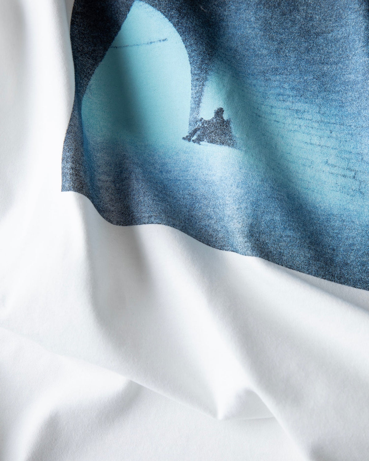Fabric close-up of the Faded artwork print on the white Faded Play T-shirt, showing the washed blue tones