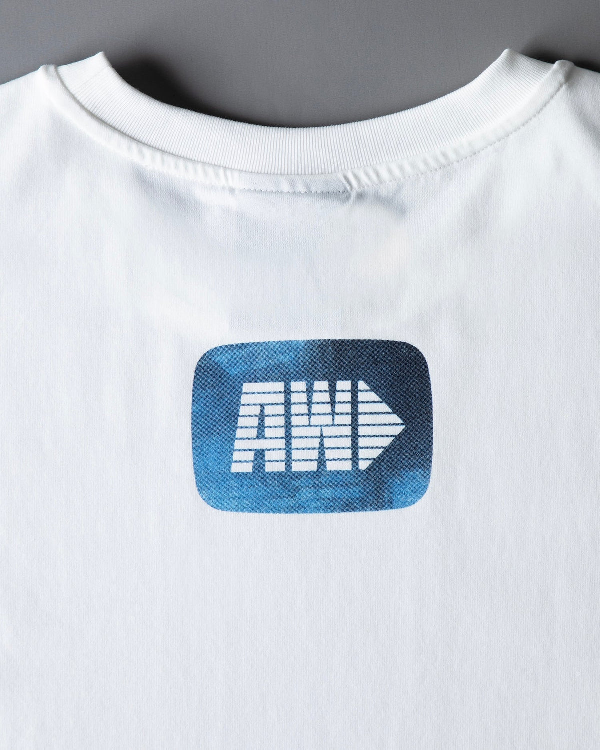 Back print close-up on the Faded Play T-shirt, the blue AW arrow logo badge below the collar
