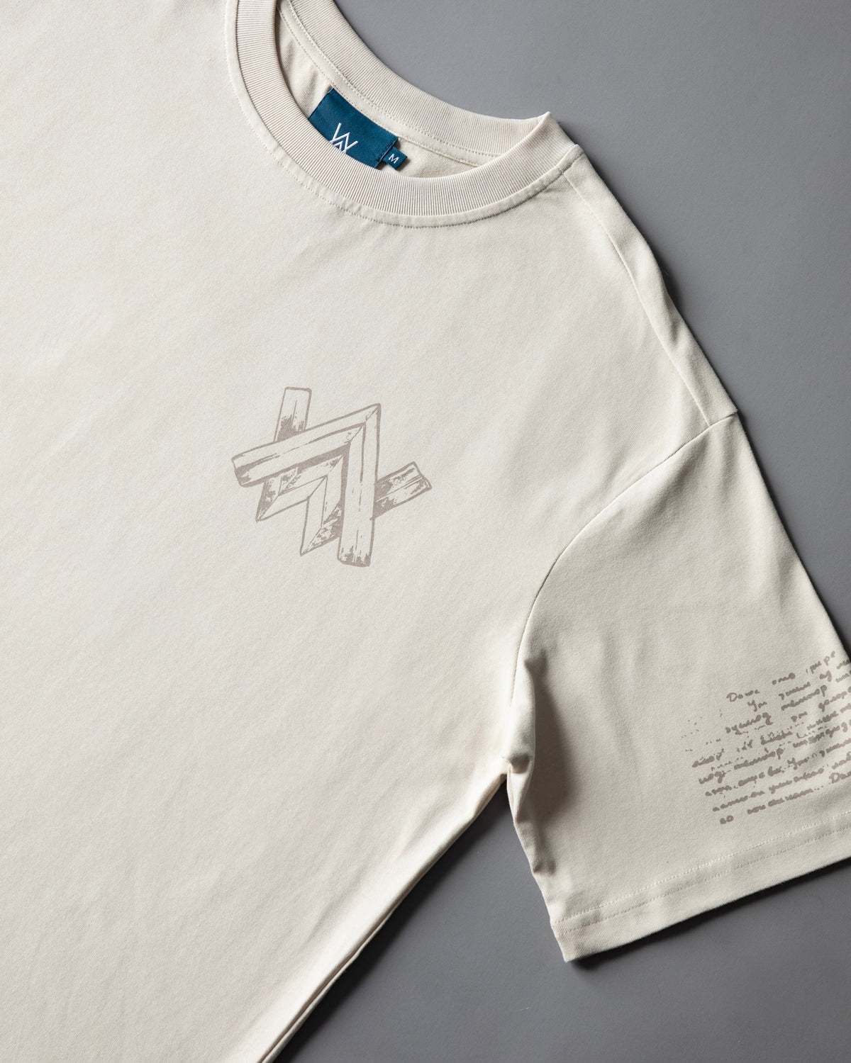 Alan Walker Encyclopedia T-Shirt in cream, angled front view with grey AW chest print and handwritten script on the sleeve