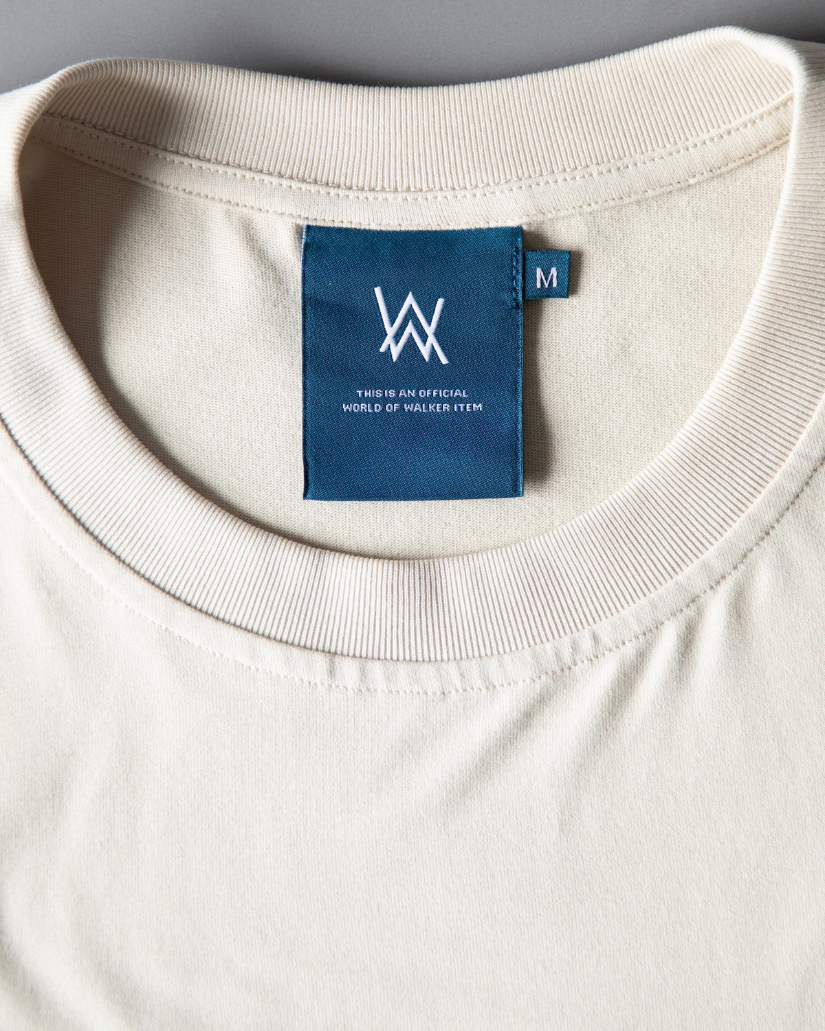Alan Walker Encyclopedia T-Shirt collar close-up, ribbed off white neckline with the teal AW inner label