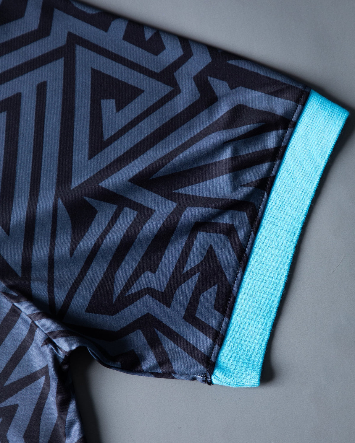 Alan Walker Gaming Jersey sleeve close-up, cyan ribbed cuff trim against the grey geometric maze print