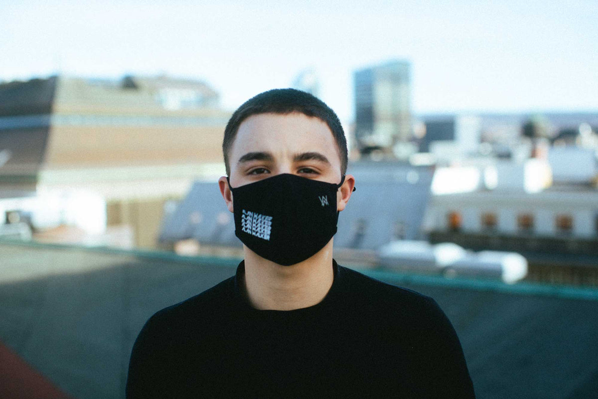Alan Walker Repeat Logo Mask worn by a model on a rooftop, black mask with blue repeat logo print