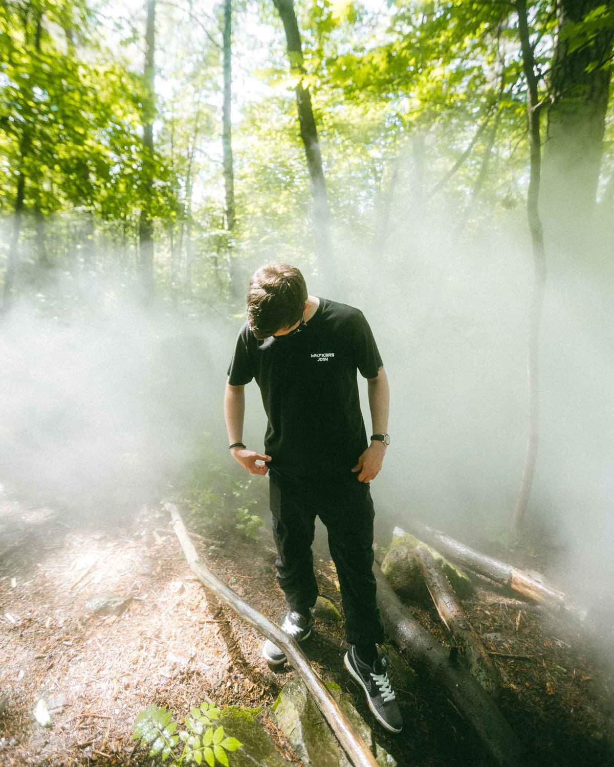 Alan Walker Core Logo T-Shirt lifestyle shot, fan in the black tee standing in fog among sunlit trees