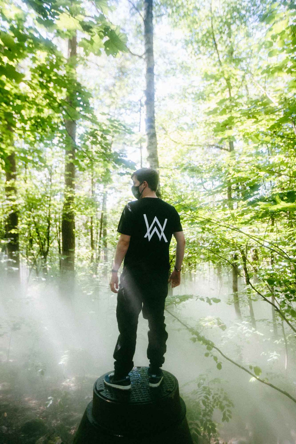Alan Walker Core Logo T-Shirt back view on a fan in a misty forest, white AW logo bright against black