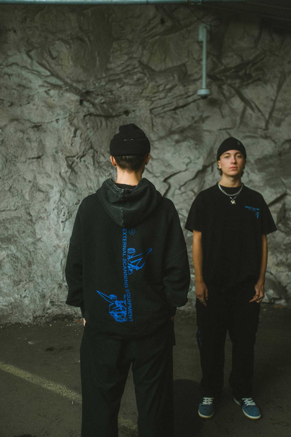 Alan Walker Drone Repair Shop Hoodie back view on a model beside a friend in the matching black tee