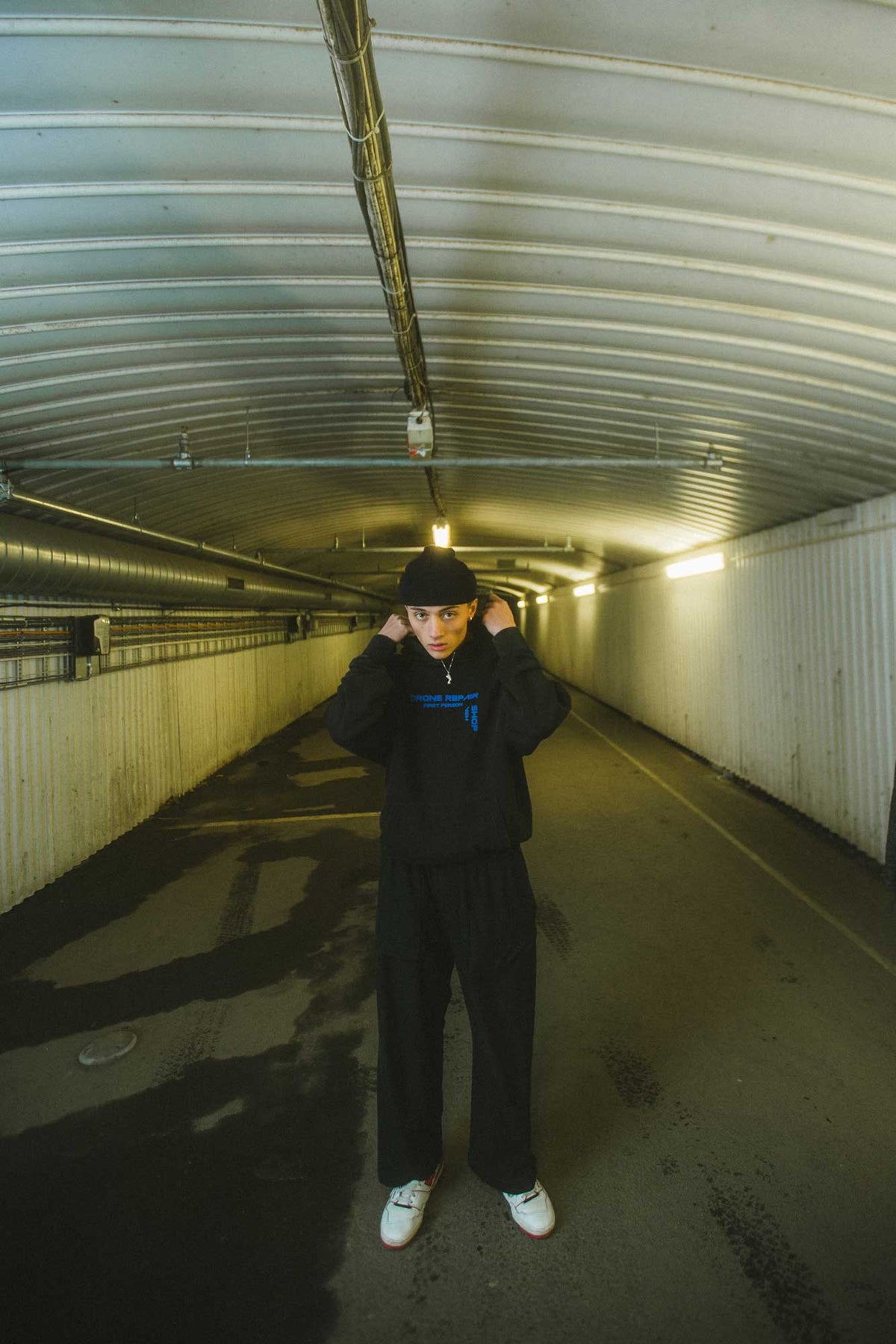 Alan Walker Drone Repair Shop Hoodie worn hood up in a lit underpass