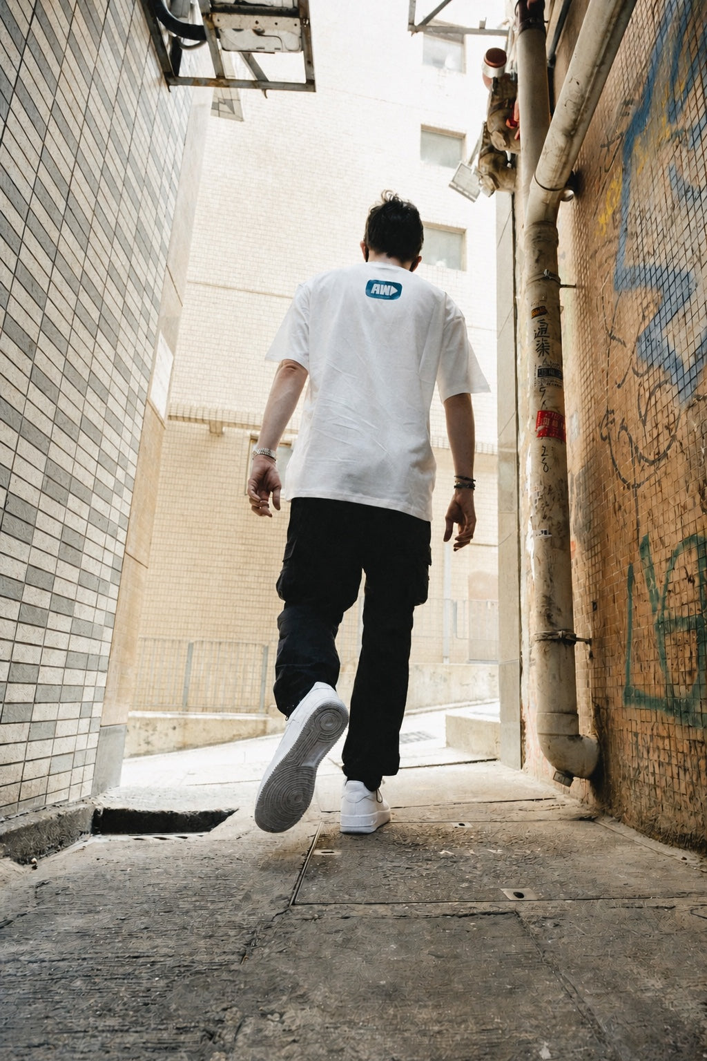 Model walking away down a graffiti alley in the Faded Play T-shirt, back AW logo print in view
