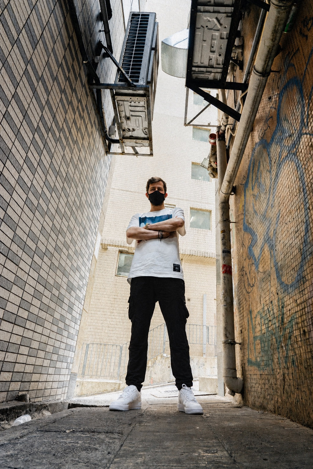 Model wearing the Alan Walker Faded Play T-shirt with black trousers, standing in a graffiti-covered alley