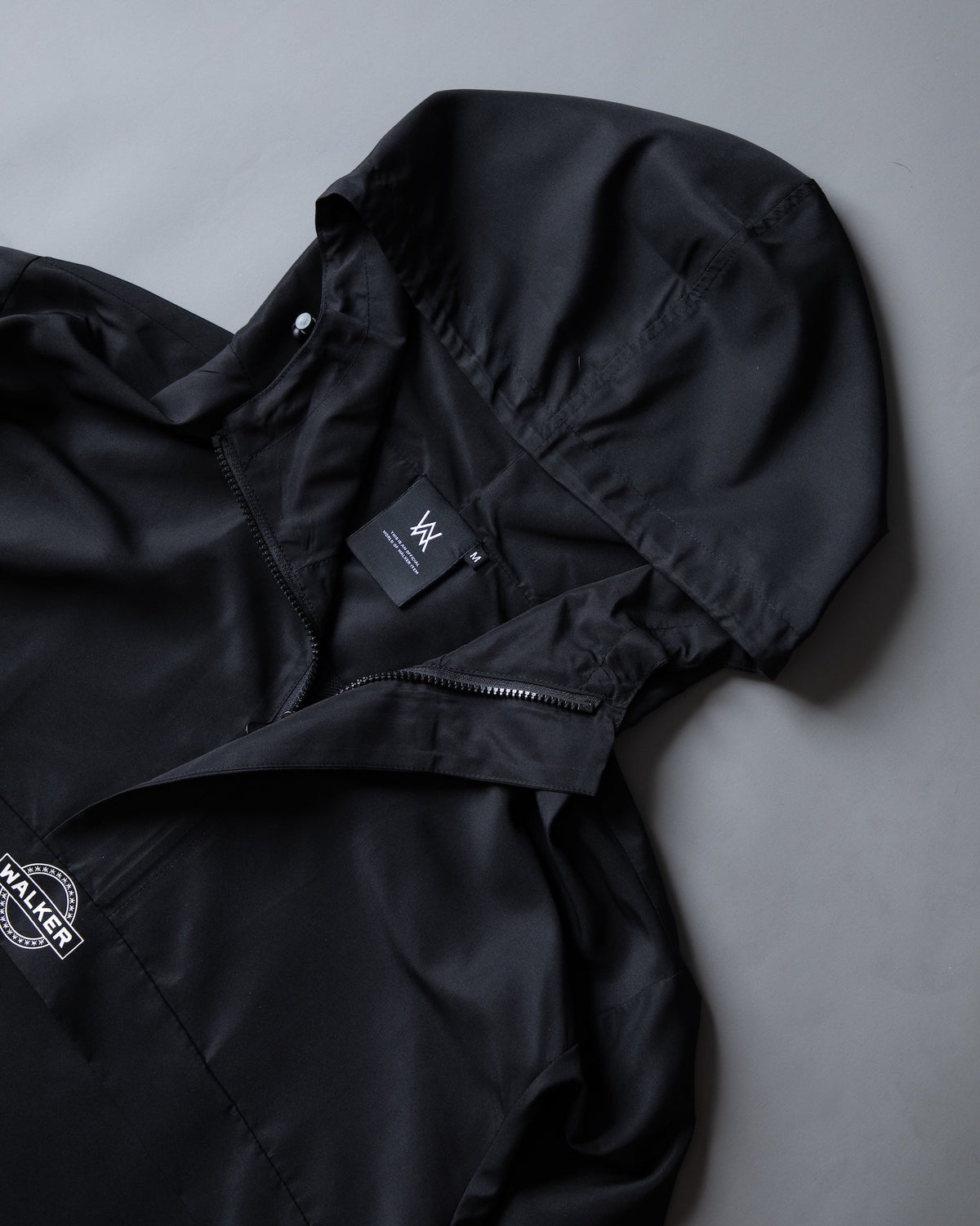 Alan Walker Core LV1 Windbreaker folded with the hood up, size tag and white Walker stamp on the hem
