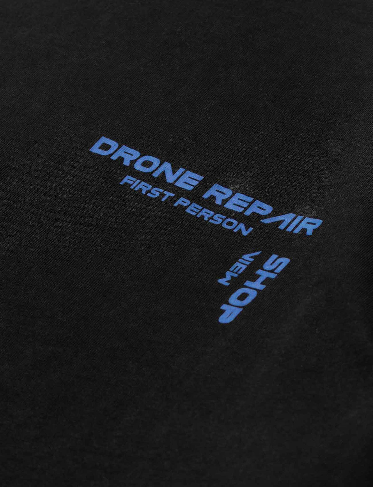 Alan Walker Drone Repair Shop T-Shirt chest print close-up, blue Drone Repair Shop lettering on black cotton