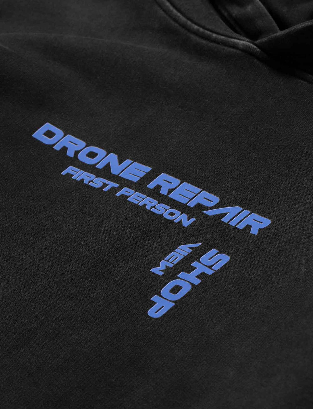 Alan Walker Drone Repair Shop Hoodie chest print close-up, blue Drone Repair Shop lettering on black fleece