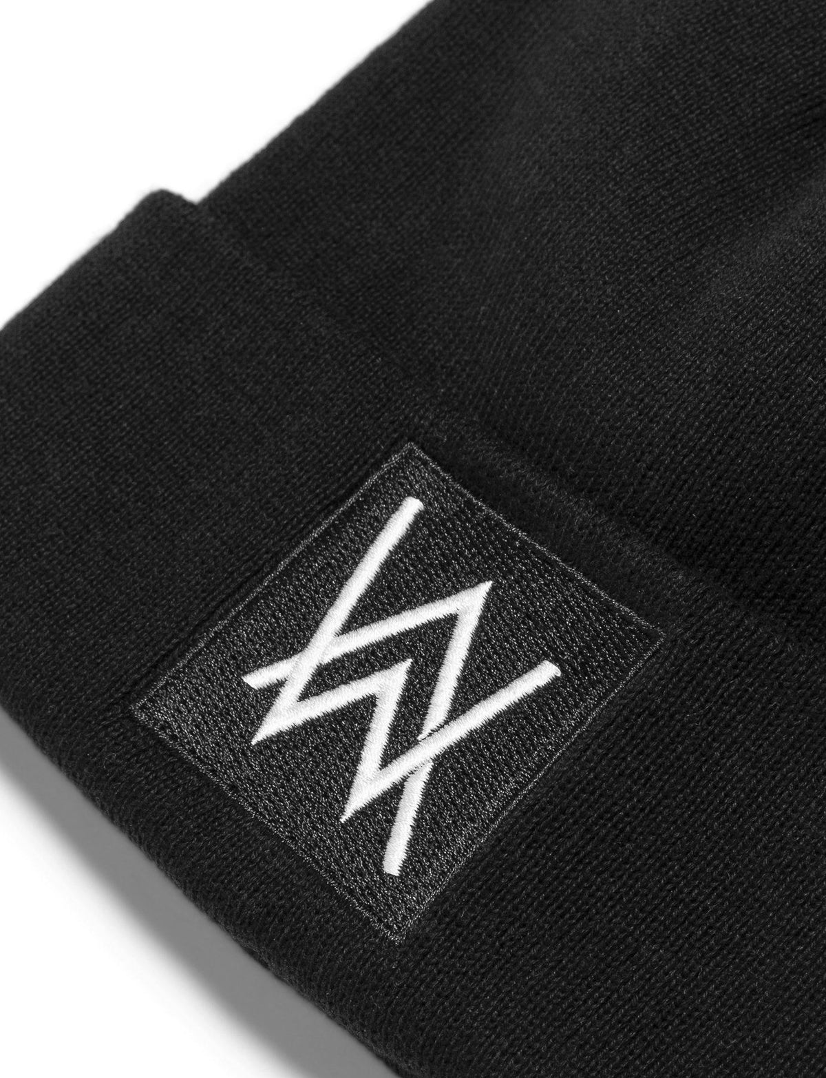 Alan Walker Core Beanie label close-up, white embroidered AW logo on a square patch over ribbed black knit