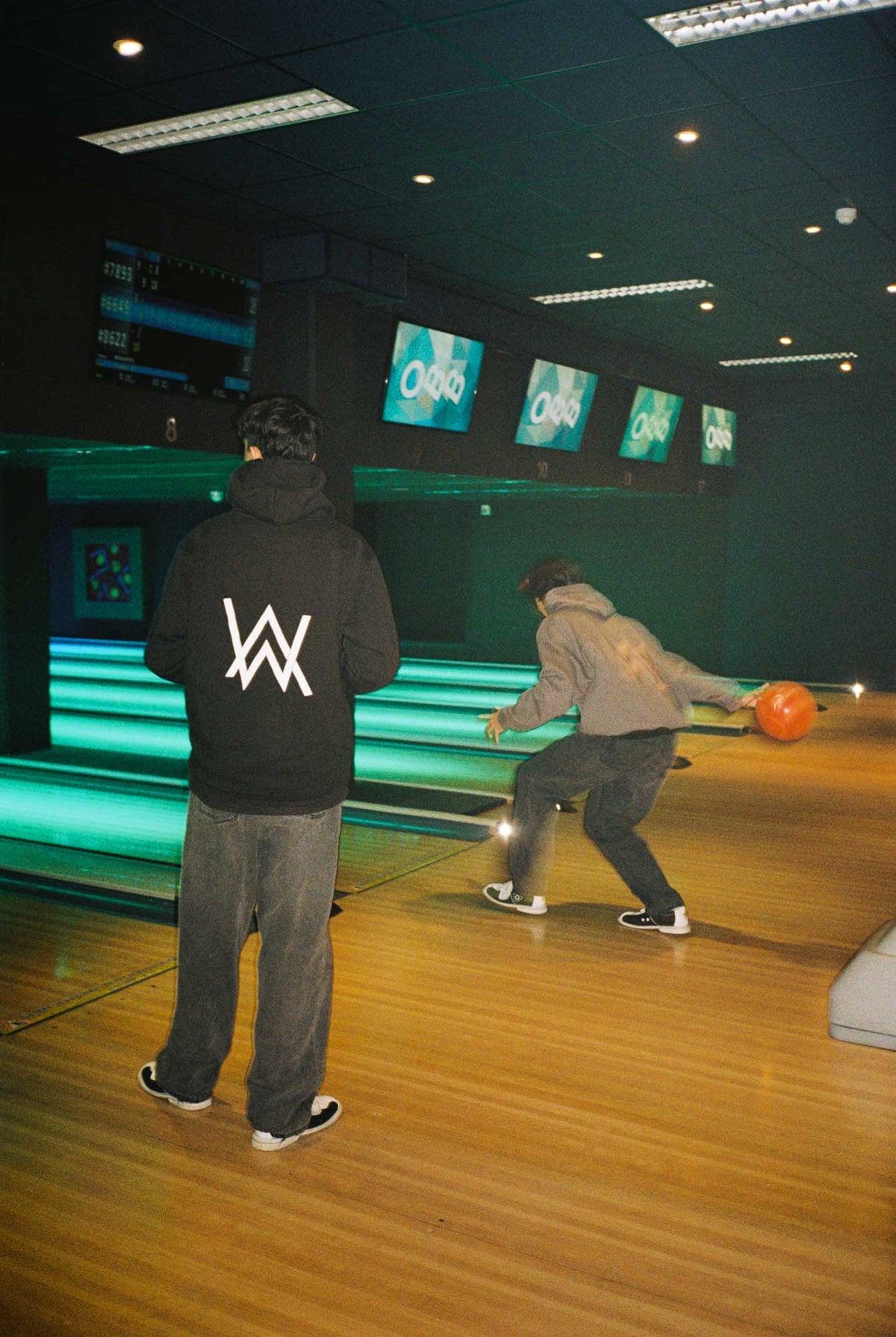 Alan Walker Core Logo Hoodie worn at a bowling alley, white AW back logo glowing under the neon lanes