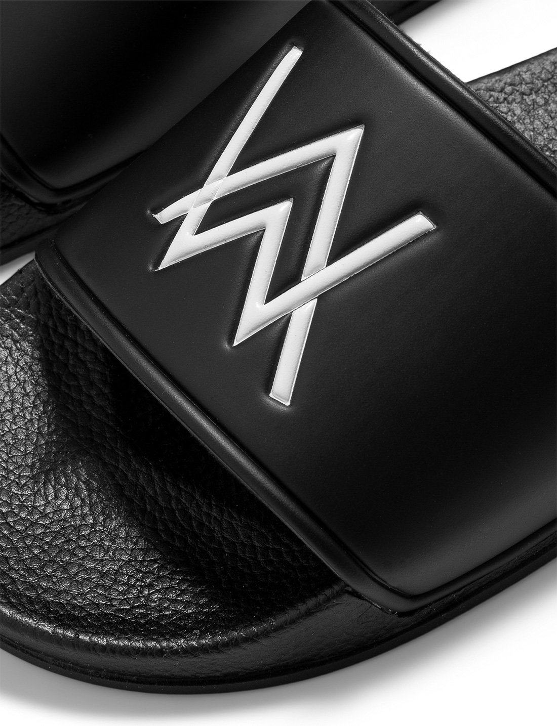 Alan Walker Logo Slippers close-up of one black slide, raised white AW logo on the smooth strap over a textured footbed