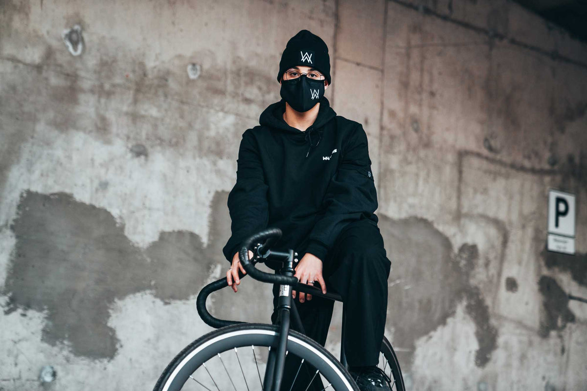 Alan Walker Core Beanie worn with a black mask by a cyclist leaning on a bike against a concrete wall