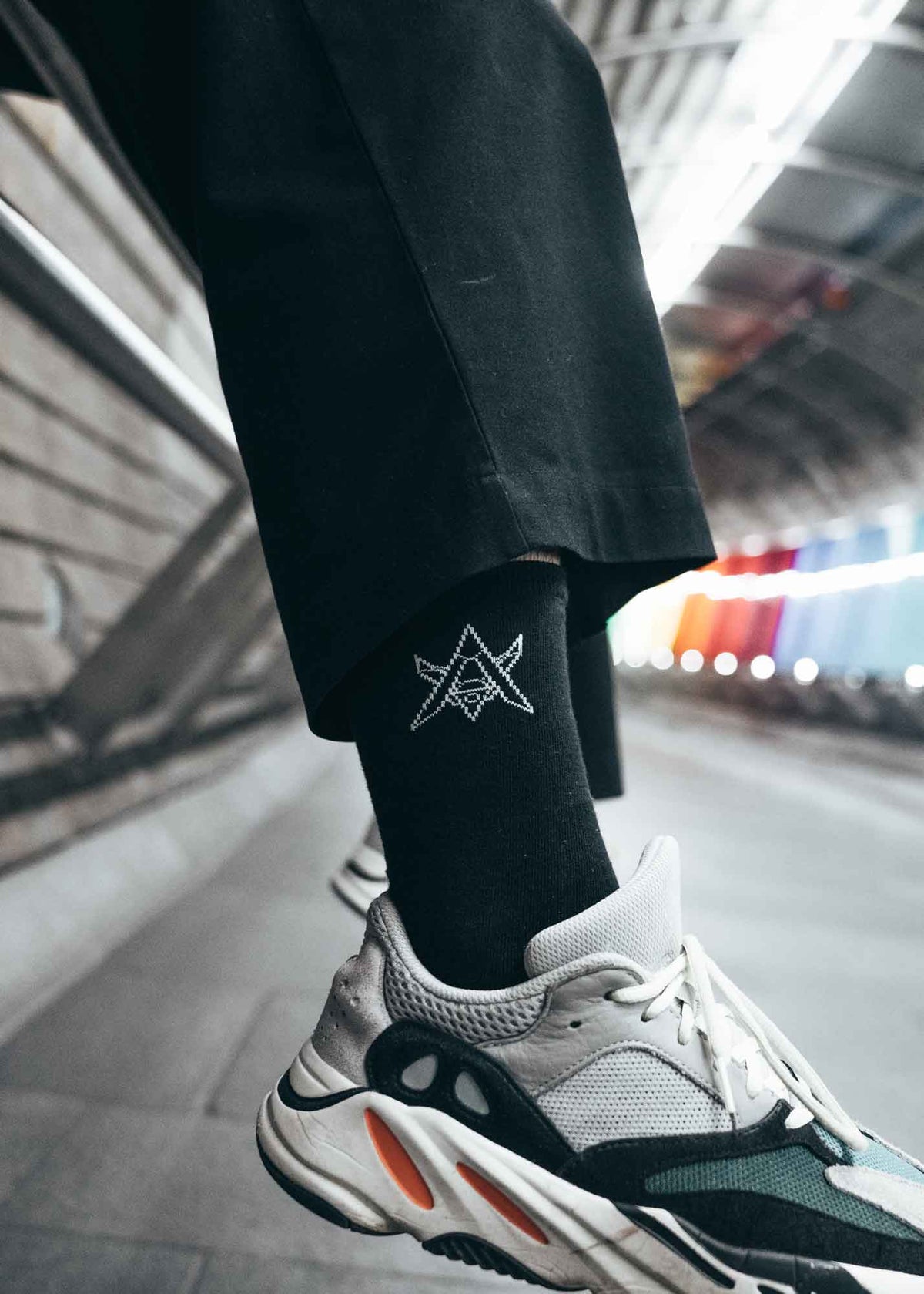 Alan Walker Drone Socks worn with white sneakers and black trousers in a lit walkway lifestyle shot