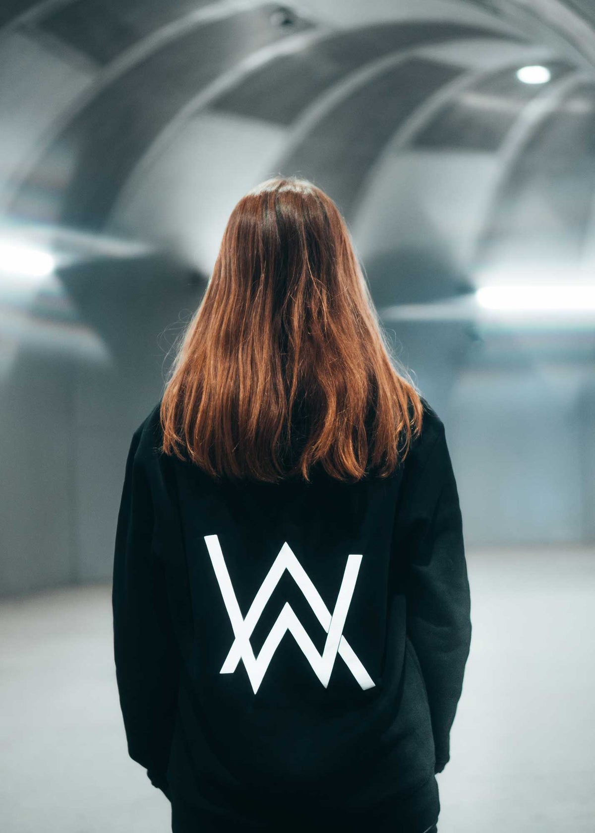 Alan Walker Core Logo Hoodie back view on a fan in a lit tunnel, bright white AW logo on black fleece