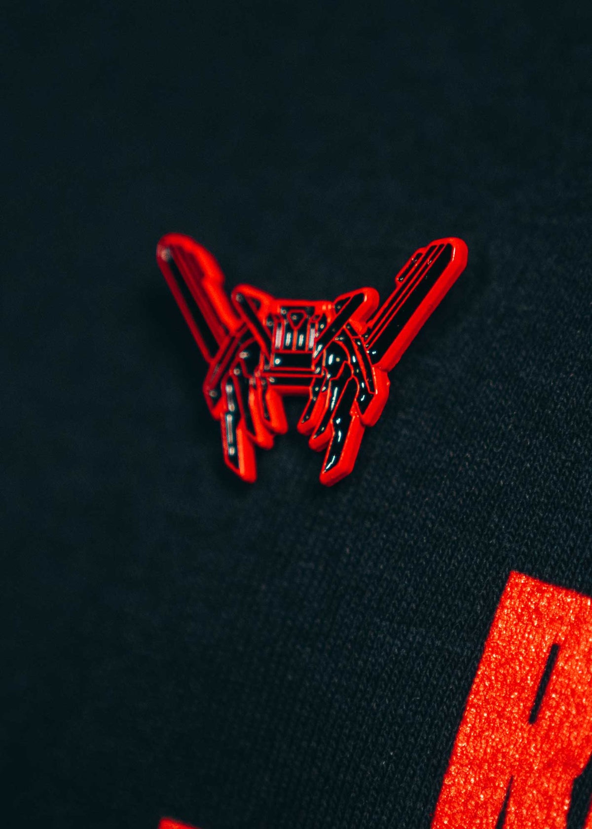 Alan Walker RX-8 Pin worn on a dark garment, red enamel drone badge catching the light beside an orange print
