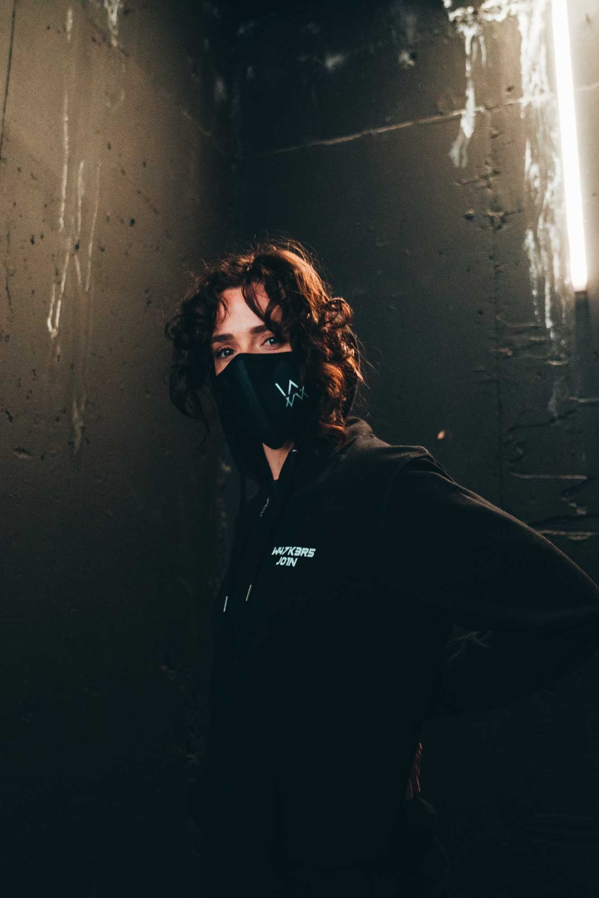 Alan Walker Core Logo Zip Hoodie worn in a dark alley with an AW face mask, white chest text catching light