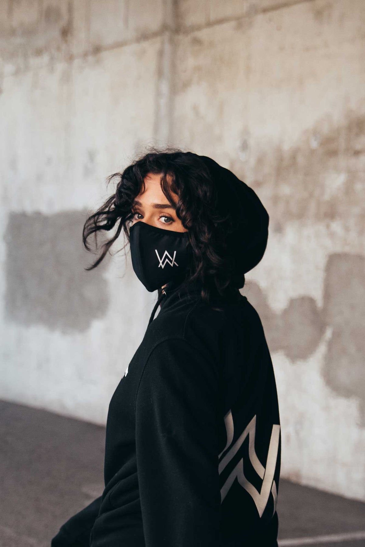 Alan Walker Core Logo Face Mask on a model in a black hood turning to camera, AW logo on the mask front