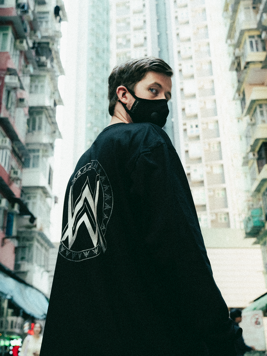 Alan Walker Monster Core Longsleeve worn by a masked model turning to show the AW crest, city high rise backdrop